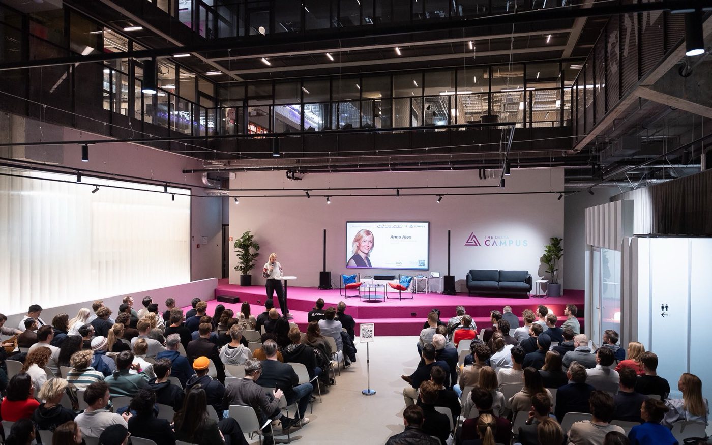 A conference keynote in the Atrium, the speaker at a lectern before the wall screen